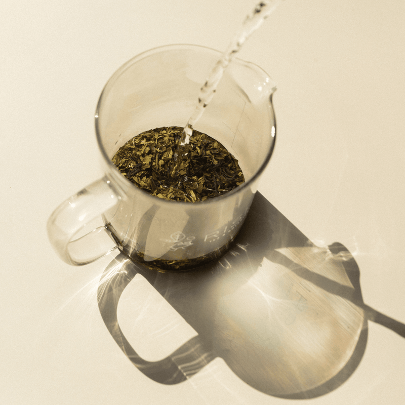 Hot water is poured into a glass pitcher with loose leaf vanilla licorice tea from Rishi Tea & Botanicals, casting a distinct shadow on a light surface.