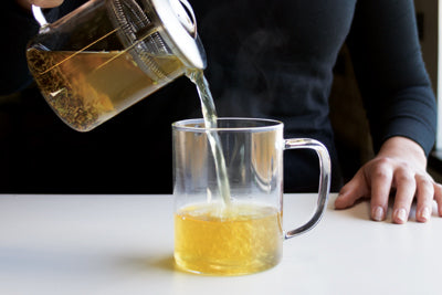 Pouring fresh loose leaf tea into a glass mug