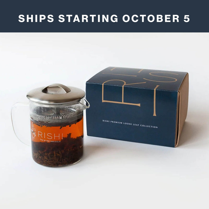A glass teapot filled with loose leaf tea sits beside a blue Rishi Tea gift box. Text above reads, “Ships starting October 5.”.