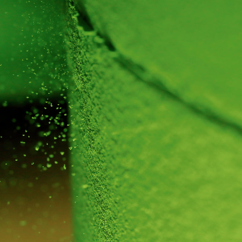 Close-up of a bright green textured surface with fine powder or granules clinging along a vertical edge, against a matching green blurred background.