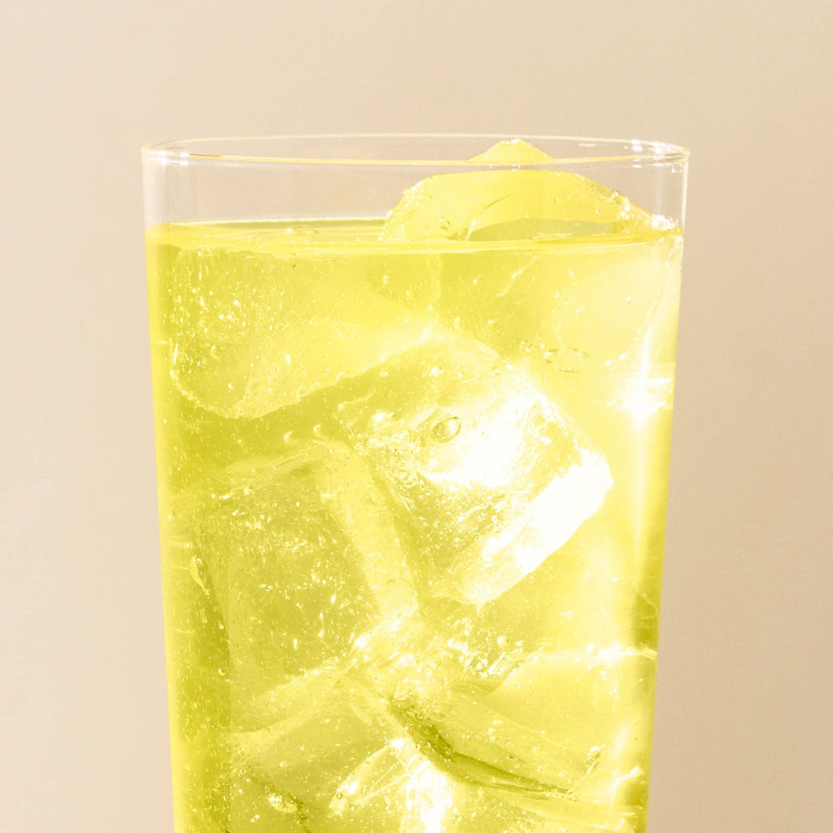 A clear glass filled with yellow-green matcha and large ice cubes from Rishi Tea & Botanicals sits against a plain, light background.