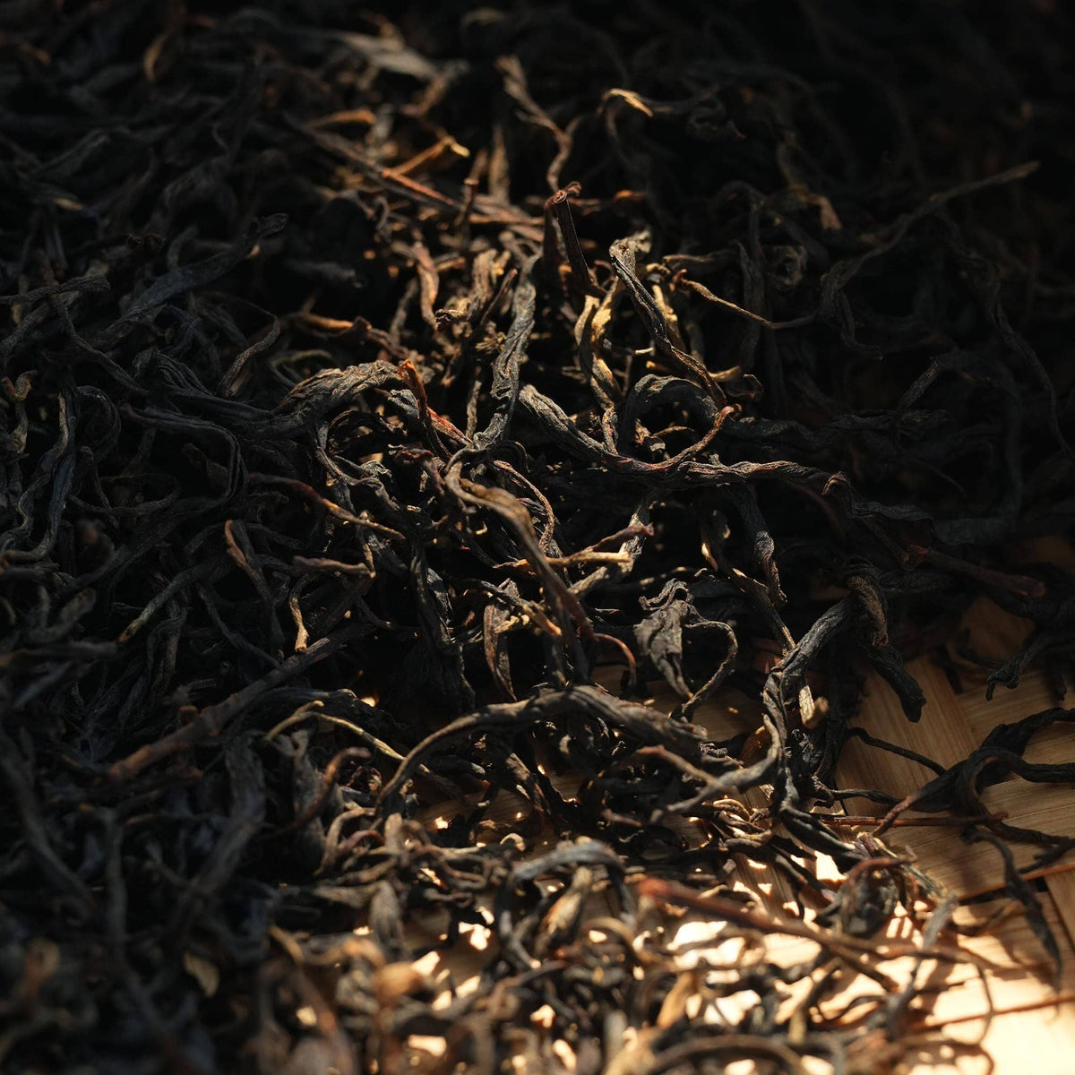 Loose-leaf black tea from Rishi Tea & Botanicals scattered on a wooden surface, partially illuminated by natural sunlight.