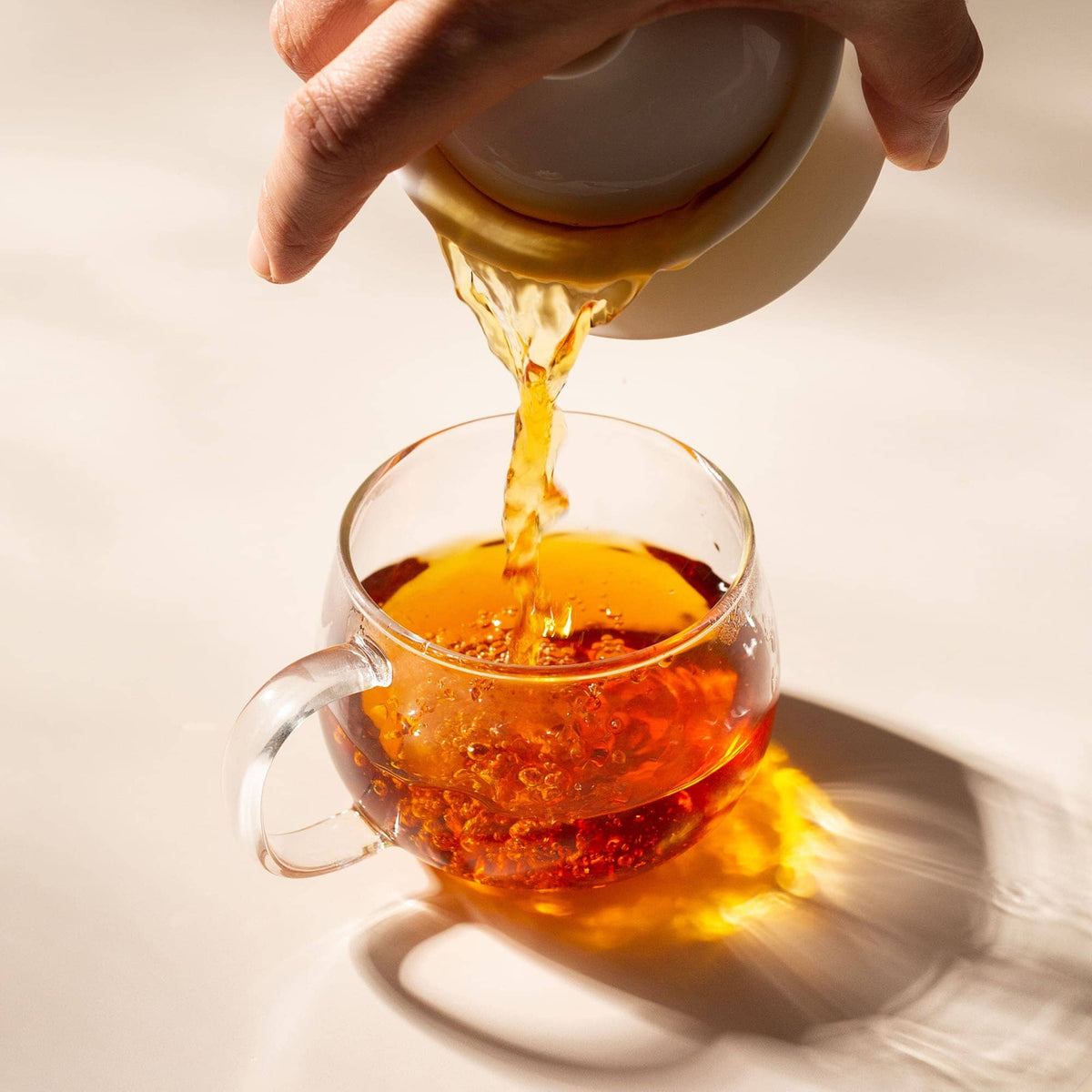 Tea being poured from a teapot into a glass cup on a light background
