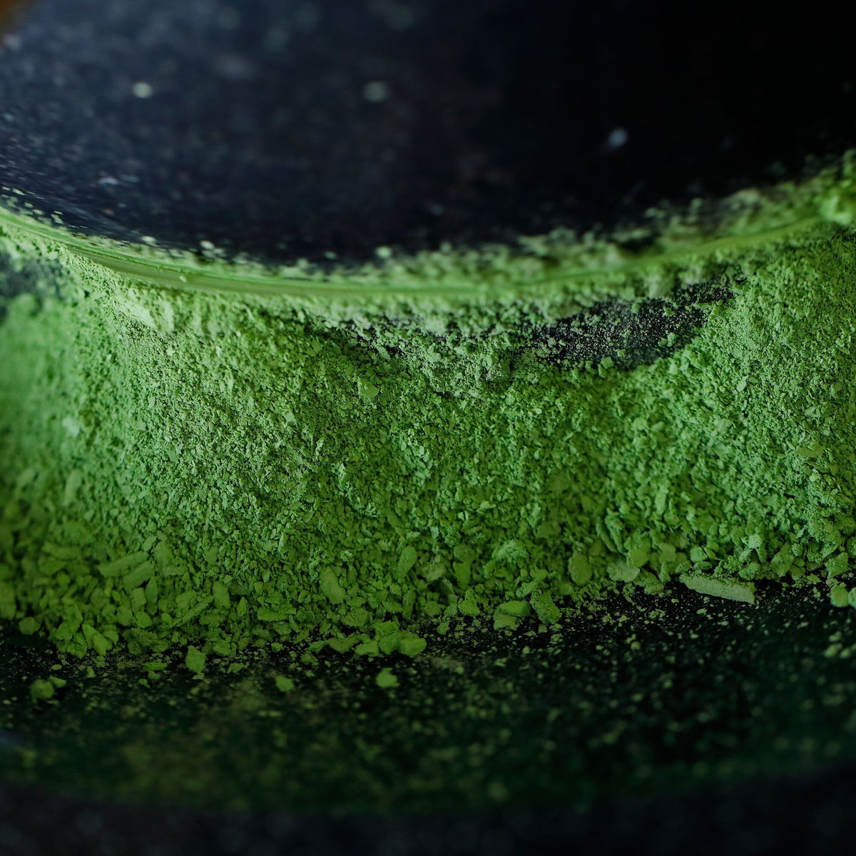 Close-up of vibrant green Kyoto matcha powder from Rishi Tea & Botanicals, possibly blended cultivars, spread unevenly on a dark surface.