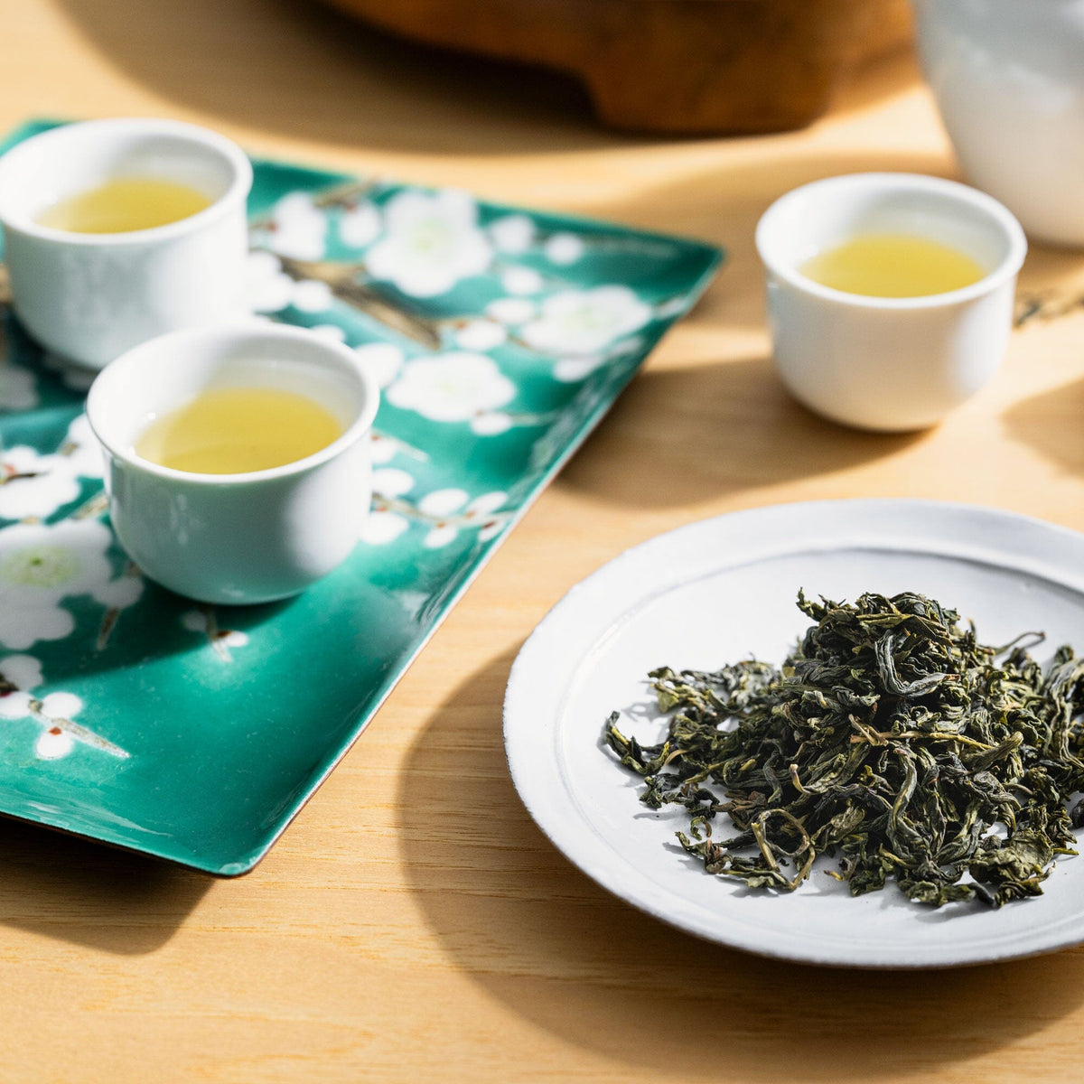 Two cups of Bao Zhong tea on a plate next to a bowl of Rishi Tea & Botanicals green tea.