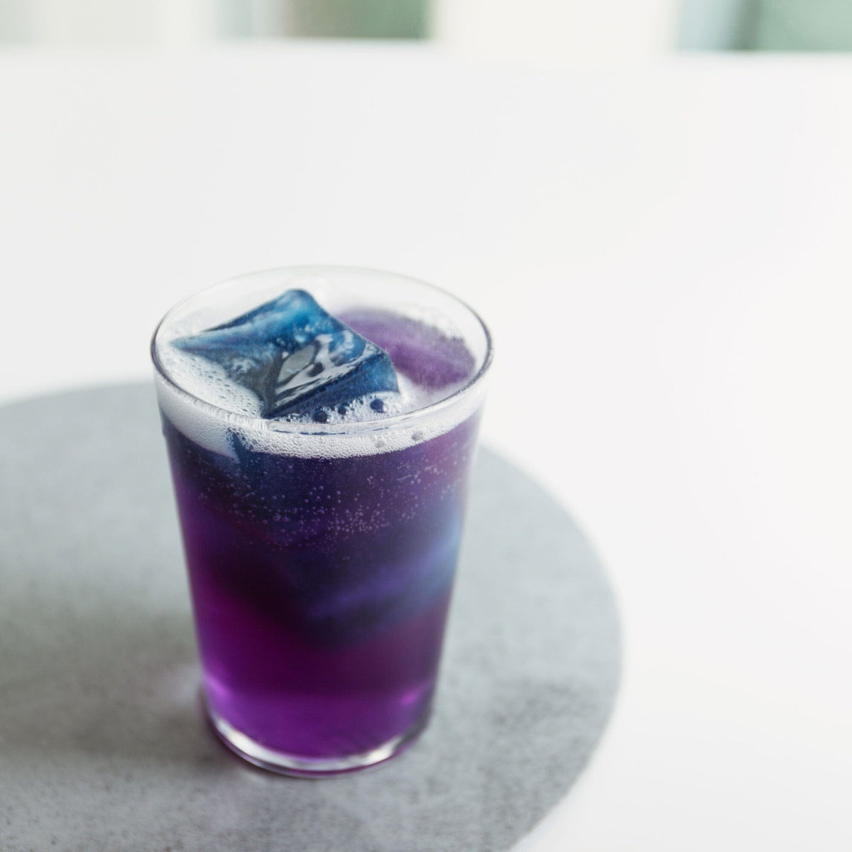 A purple Butterfly Pea Flower Powder drink with ice cubes sitting on top of a table made by Rishi Tea & Botanicals.