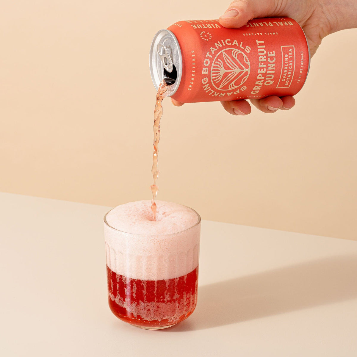 A hand pours a can of Rishi Tea & Botanicals sparkling grapefruit quince juice into a glass, forming a delicate foamy layer on top.