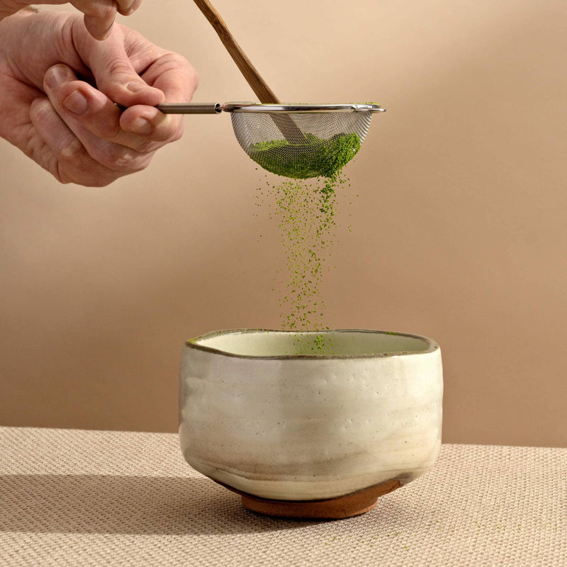 A person is pouring 21oz of Wabi Sabi Raku Matcha Bowl from Rishi Tea & Botanicals into a bowl.