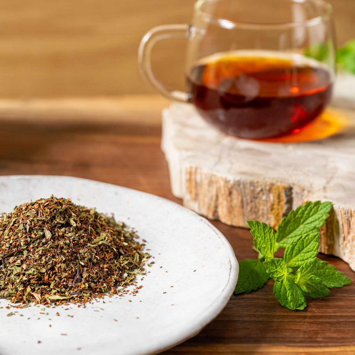 A white plate with a cup of Rishi Tea & Botanicals' Peppermint Rooibos and a handful of herbs.