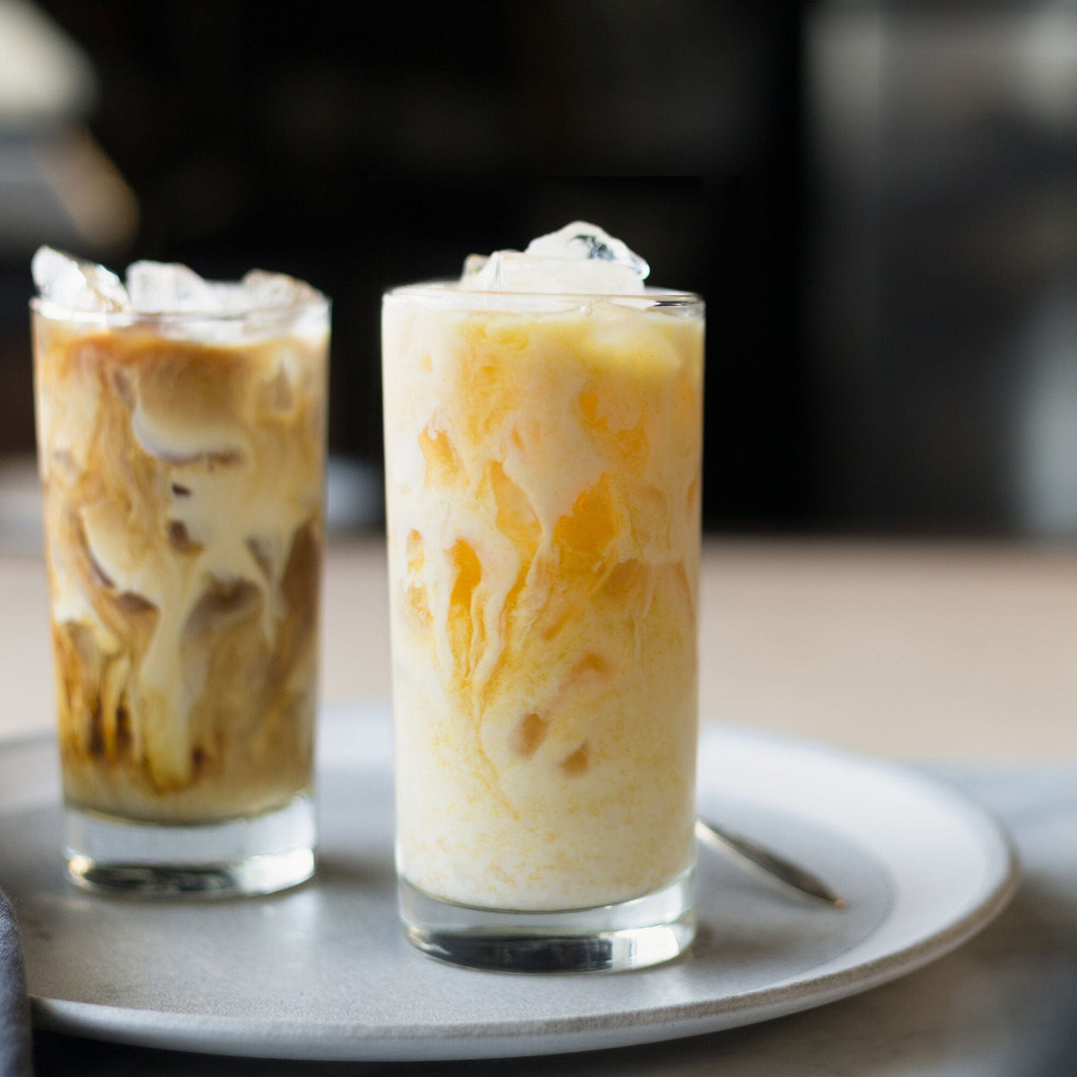 Two glasses of iced Masala Chai latte on a plate, showing layers of milk and Rishi Tea & Botanicals Concentrate Sampler Pack.