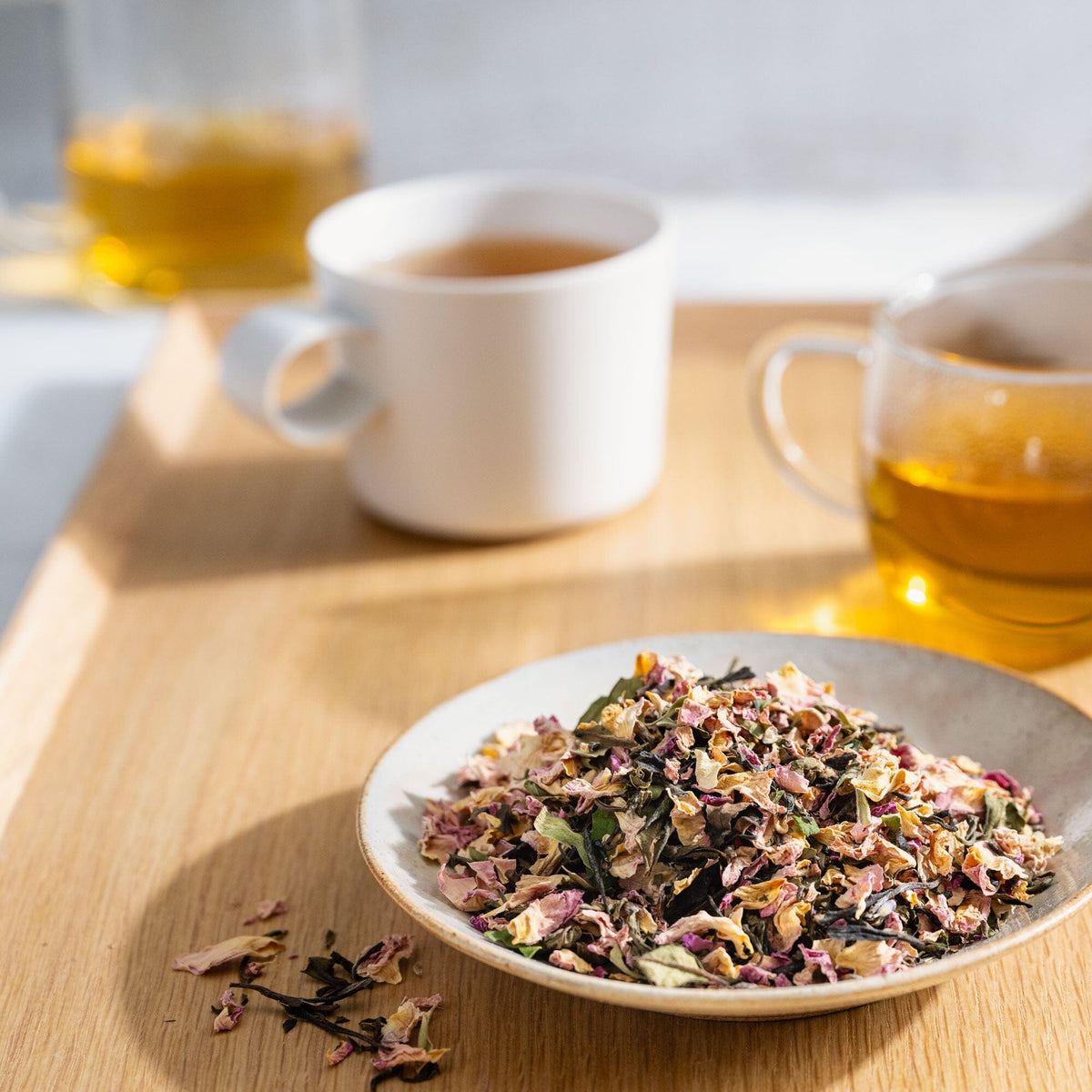 A bowl of White Tea Rose Melange on a tray next to a cup of White Tea Rose Melange. (Brand Name: Rishi Tea & Botanicals)