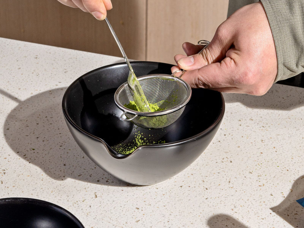 Person straining Chato Co., Ltd.'s Everyday Matcha Sifter through a stainless steel mesh sifter into a black bowl.
