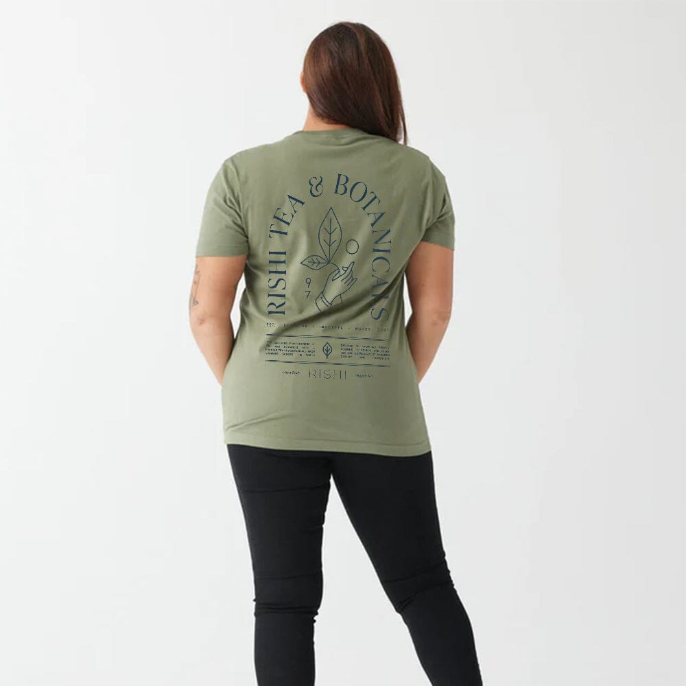 A person wearing the Rishi Weekend T-Shirt - Olive Green, made from organic cotton with "Rishi Tea & Botanicals" text and a leafy design on the back, paired with black pants, standing against a plain background. This unisex shirt is comfortable for all and embraces Fair Trade certification.