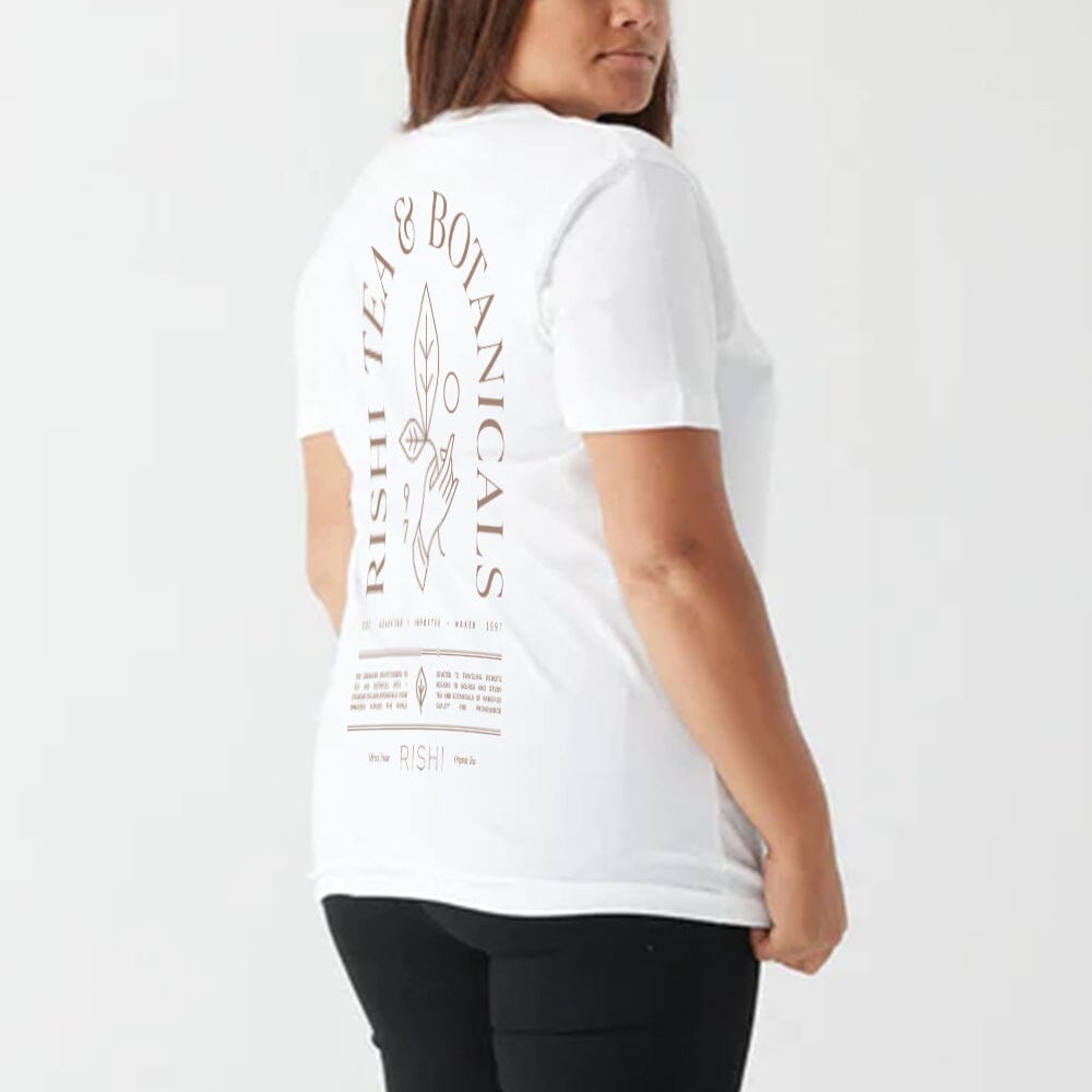 A person is wearing the Rishi Weekend T-Shirt - White, made of organic cotton with "Rishi Tea & Botanicals" and related designs printed on the back, available in unisex sizing.