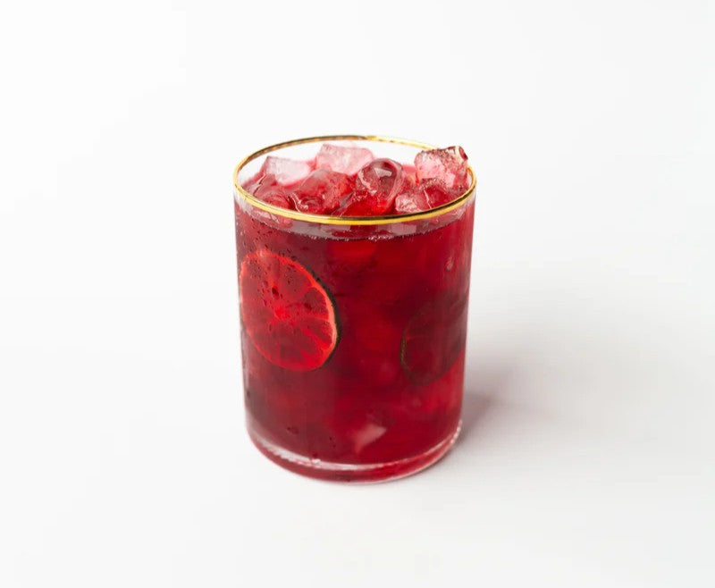 Red cocktail with ice and slices of fruit in a glass on a white background