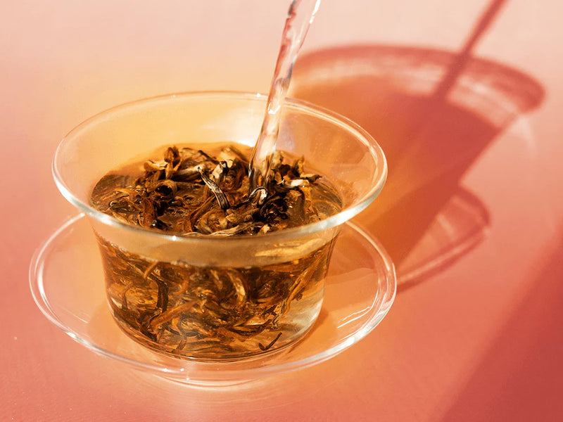 Tea being poured into a glass teacup on a pink background