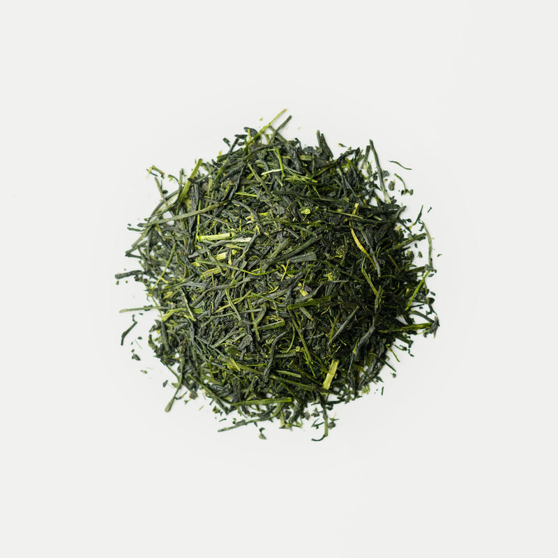 A pile of loose organic shincha green tea leaves from Rishi Tea & Botanicals on a white background, picked in early spring for a fresh, vibrant flavor and prized for its emerald-green liquor.