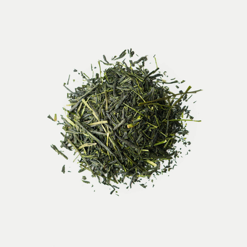 A pile of Rishi Tea & Botanicals organic Shincha loose-leaf green tea rests on a plain white background, featuring a deep umami flavor and delicate floral aroma.