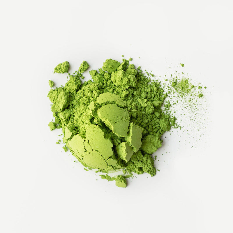 A heap of bright green Rishi Tea & Botanicals micro-lot matcha powder, scattered on a white background.