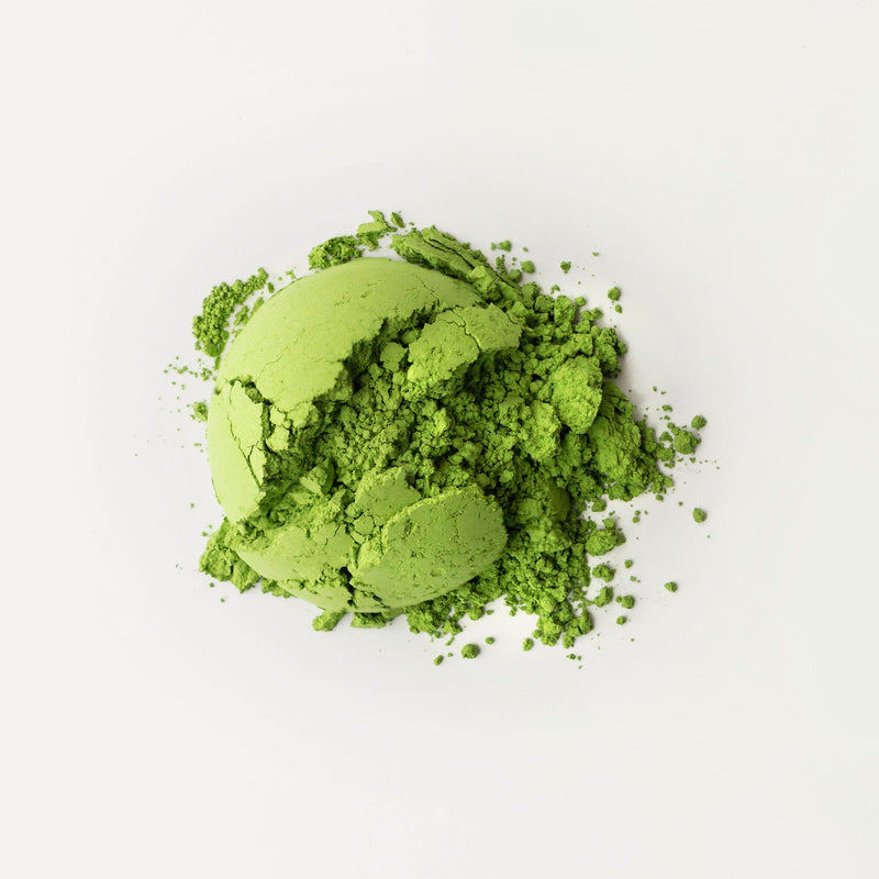 A pile of vibrant green, stone-milled organic matcha powder from Rishi Tea & Botanicals is scattered on a plain white background.