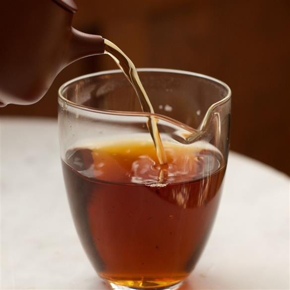 A cup of tea being poured into a Rishi Tea & Botanicals Glass Tea Serving Pitcher.