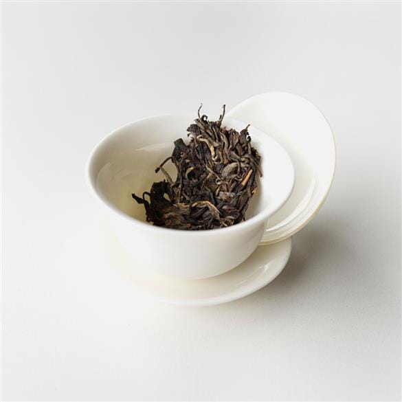 A white Kokang Gold Leaf cup filled with Rishi Tea & Botanicals tea leaves on a white surface.