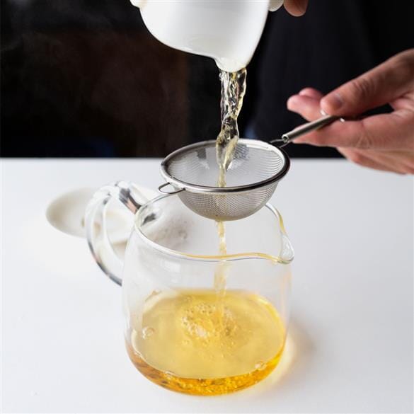 A person pouring Laos Sheng Pu’er Tea Cake Vintage 2021 from Rishi Tea & Botanicals into a glass pitcher.